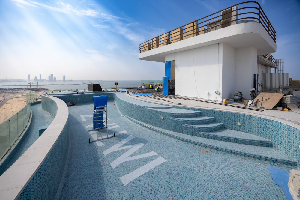 Beach Walk Residence A large unfinished rooftop pool with a view of the city skyline and construction workers nearby.